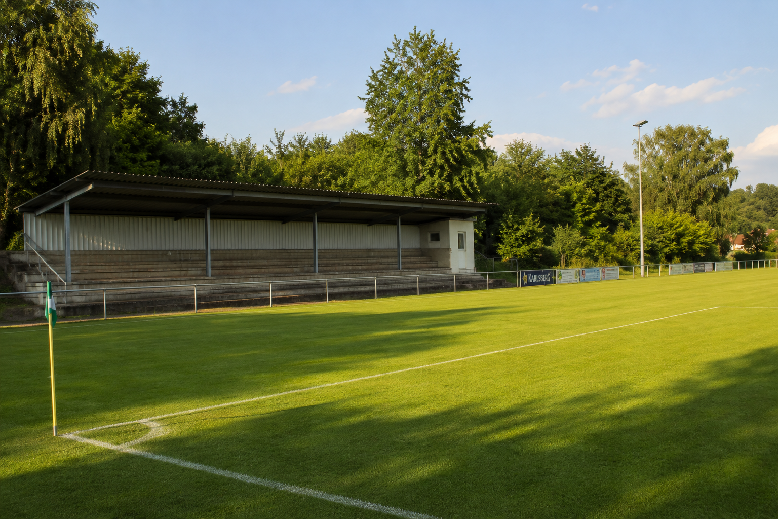 Sportplatz Gersweiler im Nachmittagslicht, gepflegter Rasen mit Tribüne und Bäumen